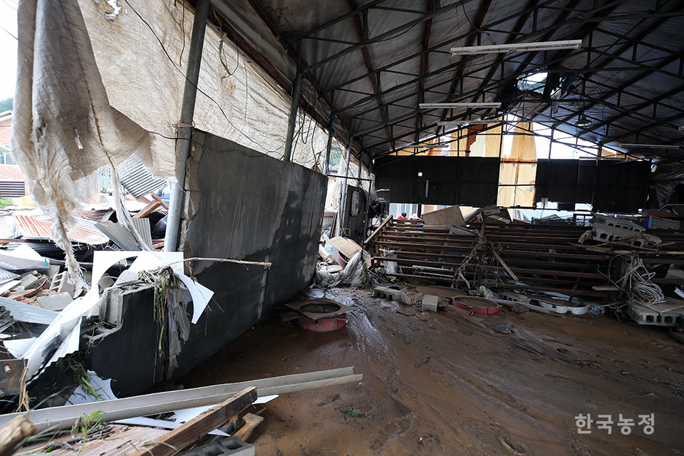 집중호우에 이은 하천 범람으로 망가진 농기계 창고에서 주민들이 피해 복구 작업을 하고 있다.