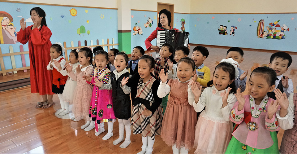 아이들이 선생님의 아코디언 반주에 맞춰 율동을 하면서 노래를 부르고 있다.
