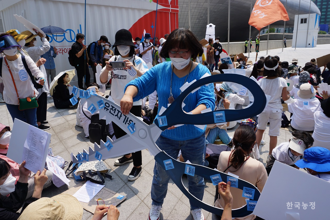 지난 21일 서울 동대문디자인플라자 앞에서 2022 몬산토·바이엘 GMO반대 시민행진 참가자들이 집회 막바지에 '유전자가위'를 상징하는 모형 가위에 'GMO OUT'이라 적힌 스티커를 붙이고 있다.