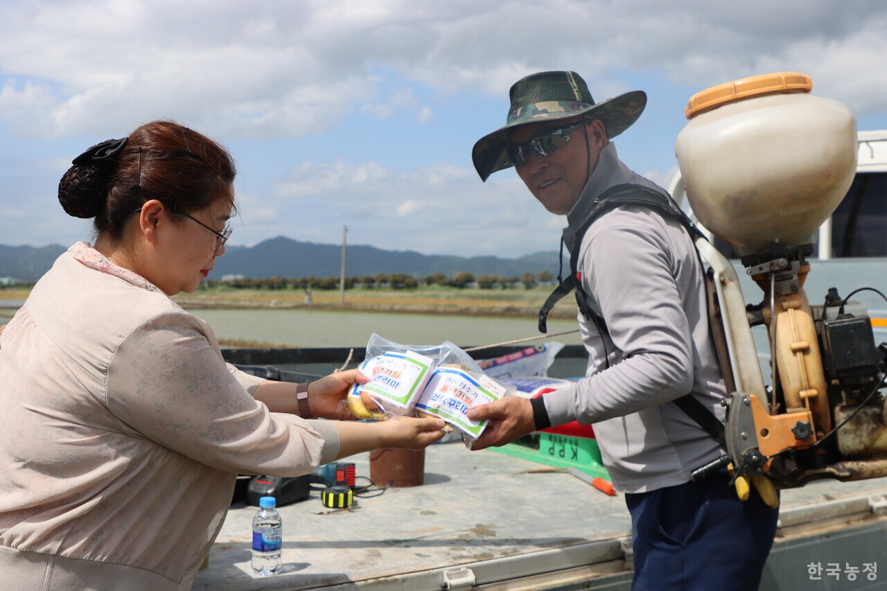 강진농협 직원 공란(왼쪽)씨가 지난 16일 전남 강진군 강진읍 들판에서 농작업 중이던 귀리 재배 농민 문학훈씨에게 ‘영농 성수기 풍년기원 간식 꾸러미’를 전달하고 있다.