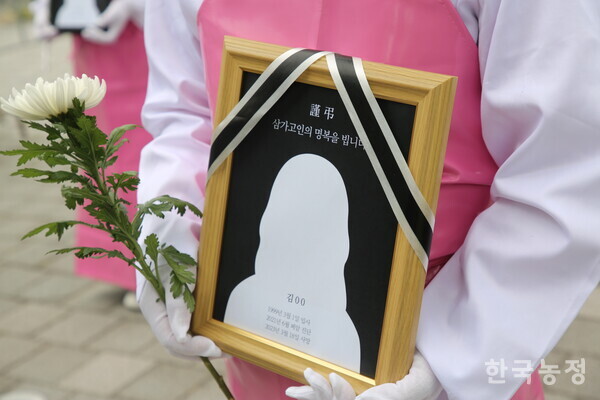 전국학교비정규직노동조합 학교급식법 개정 촉구 기자회견 참가자가 산재로 사망한 급식 노동자의 영정과 국화를 들고 있다.