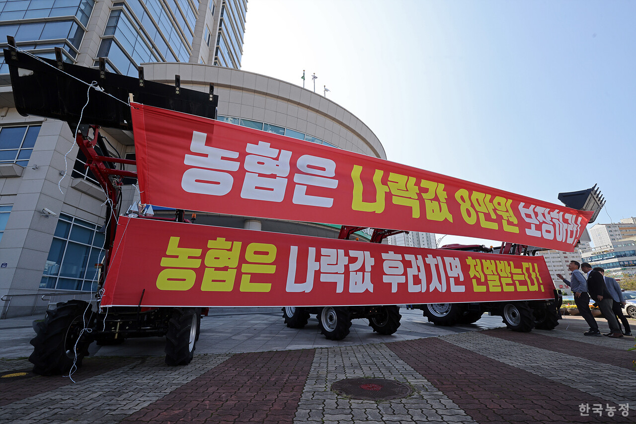 전국농민회총연맹 광주전남연맹과 전국쌀생산자협회 전남본부 회원들이 10일 오전 전남 무안군 농협중앙회 전남지역본부 앞 대로에서 ‘나락값 8만원 쟁취 농기계 행진’ 집회를 개최한 가운데 농민들이 '나락값 8만원 보장'을 촉구하는 현수막을 농협 전남지역본부 앞에 세워 놓은 트랙터에 매달고 있다. 한승호 기자